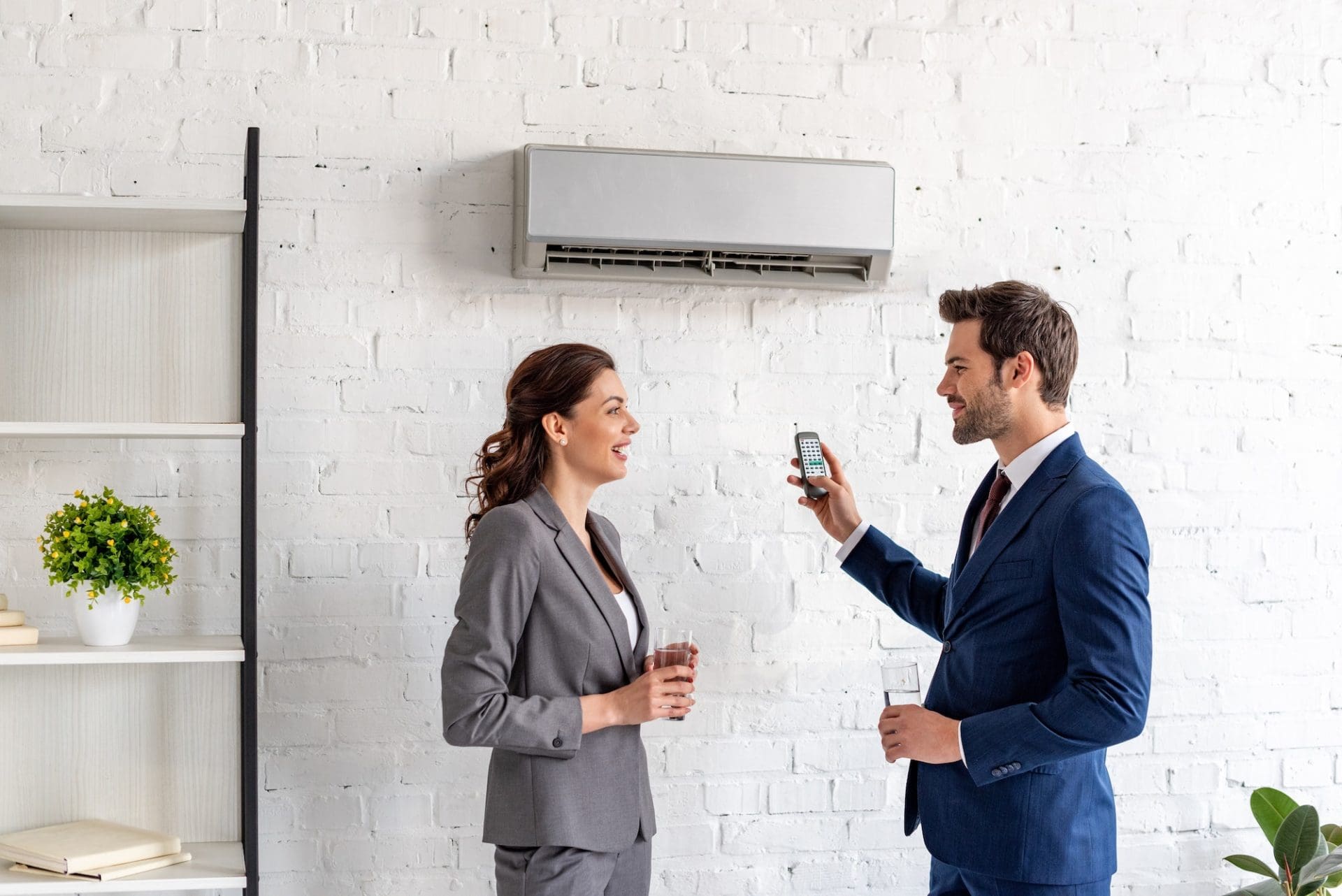 smiling businesspeople talking while standing under air conditioner in office