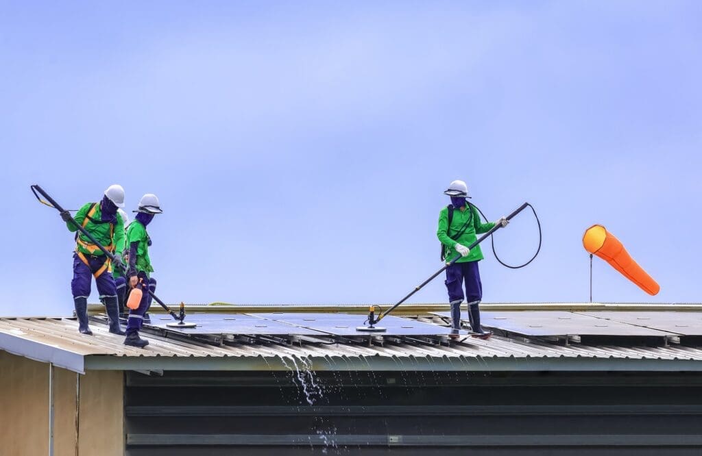 Group of professional cleaning service workers clean the solar panels on industrial building roof