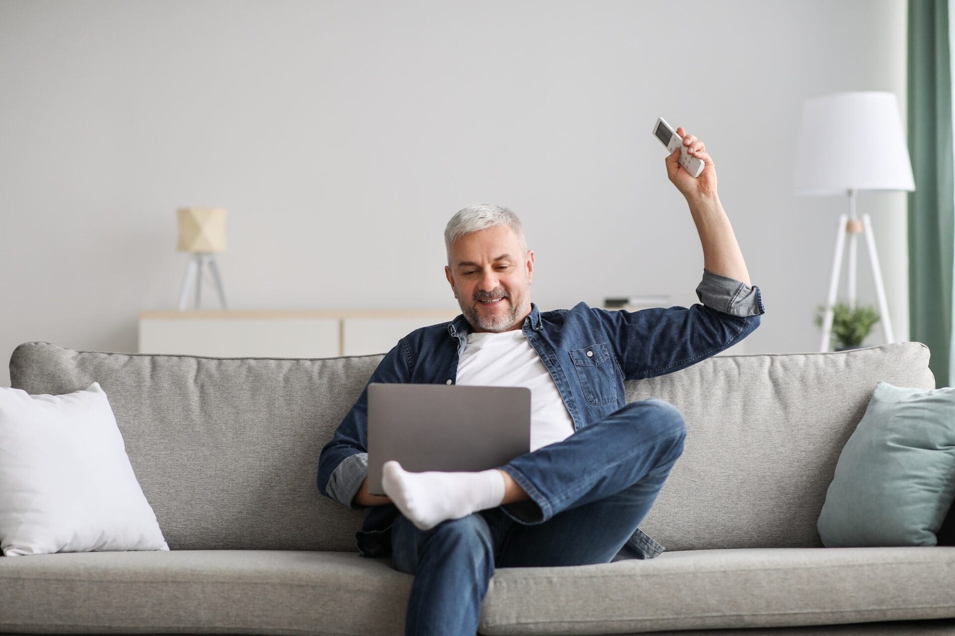 Relaxed man sitting on couch with laptop, turn on AC